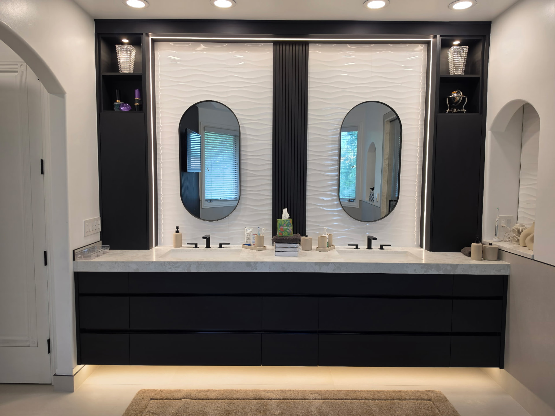 Modern floating double bathroom vanity in matte black with white marble-look counter, undermount sinks, oval mirrors and integrated LED lighting