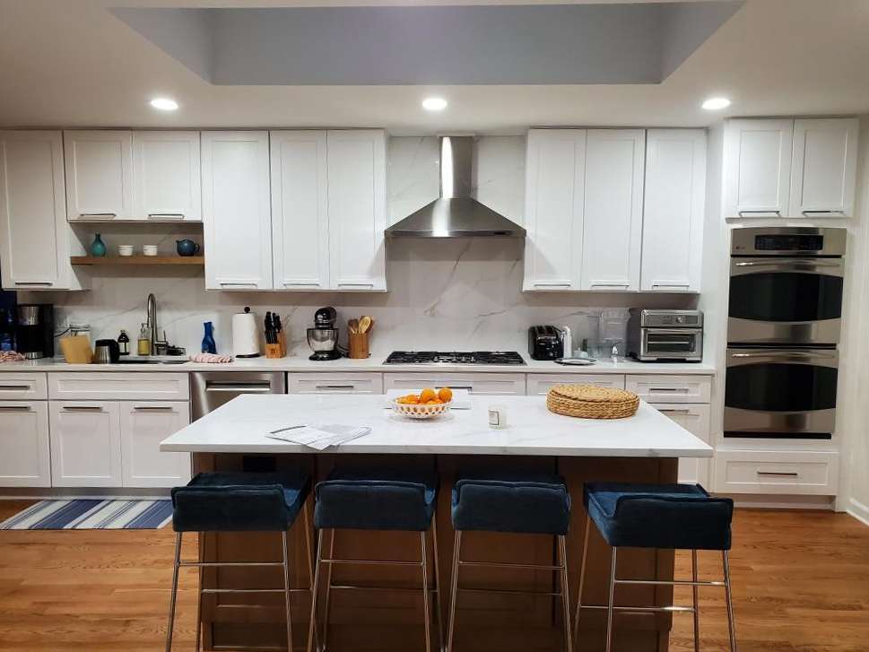 Traditional white shaker cabinetry with a wood island, marble-look counters, stainless chimney hood and nickel bar pulls