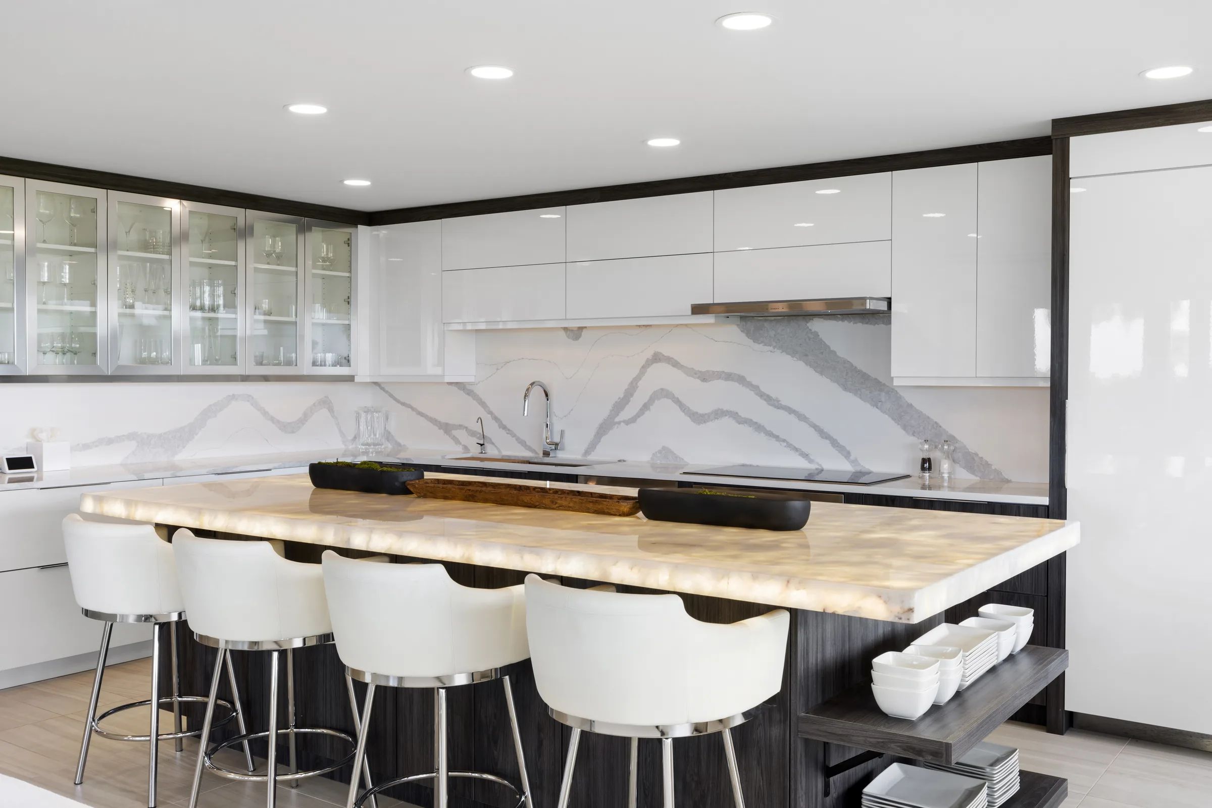 Luxury white kitchen by Bastom Inc. with a full-height marble backsplash, waterfall island and upholstered bar seating